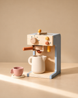 Wooden pretend play coffee machine with mug and pink cup on beige background.