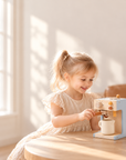 Happy little girl plays barista with wooden pretend coffee maker in a sunlit room.